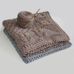 two knitted blankets and a ball of yarn on a white surface with grey background