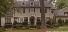 a large white house with lots of windows and bushes in front of the house is surrounded by trees