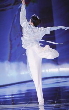 a woman in white dancing on stage with her arms out to the side and one leg up