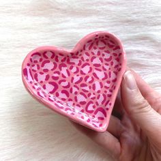 a hand holding a pink heart shaped dish