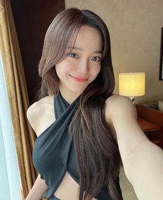 a woman with long brown hair wearing a black top and posing for the camera in front of a window