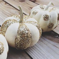 white pumpkins with gold glitter on them sitting on a wooden table next to each other