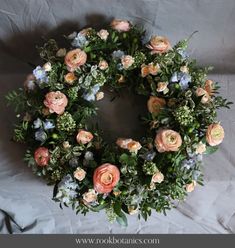 a wreath with flowers and greenery on a white sheeted surface, ready to be used as an ornament