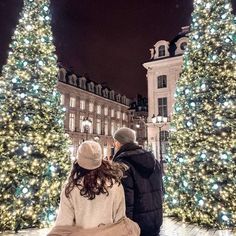 a man and woman sitting on a bench in front of a christmas tree at night