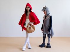 two children dressed up in costumes standing next to each other on a table with a white wall behind them