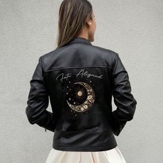 a woman wearing a black leather jacket with the moon and stars painted on it's back