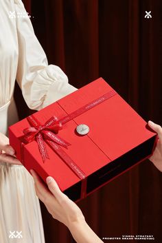 a woman holding a red box with a button on it and another person's hand