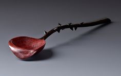 a red spoon with spikes on it sitting on a gray table next to a barbwire