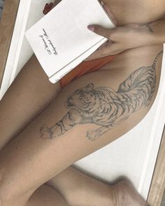 a woman with a tiger tattoo on her leg is laying down and reading a book