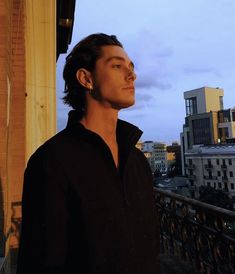 a man standing on a balcony next to a building and looking off into the distance