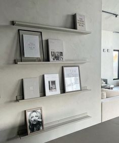 some shelves with pictures and photos on them in a room that has white walls, floor to ceiling