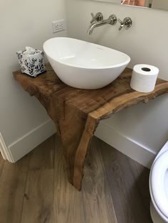 a white bowl sink sitting on top of a wooden counter next to a toilet paper dispenser