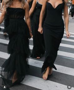 two women in black dresses walking across a street