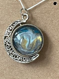 a pendant with a blue and yellow marble in the center on a brown surface next to a pair of scissors