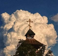 a church steeple with a cross on top and clouds in the background