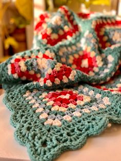 there is a crocheted blanket on top of a white table with red and blue flowers