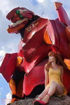 a woman sitting on top of a rock next to a giant red dragon statue in the sky