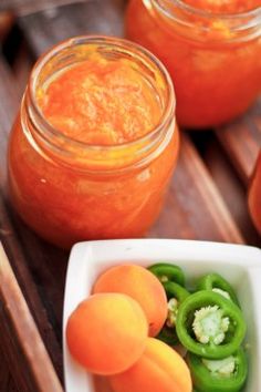 three jars filled with oranges and green peppers on a wooden table next to other food items