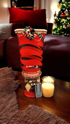 a red glass vase sitting on top of a wooden table next to a lit candle