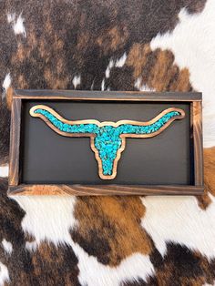 a cow skull with turquoise paint on it in a wooden frame sitting on some brown and white spots