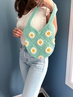 a woman holding a crocheted bag with flowers on it