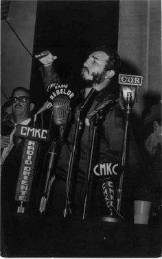 black and white photo of man speaking into microphones with other men behind him holding signs