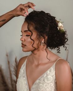 a woman is getting her hair styled by another woman with flowers in her hair and wearing a white dress