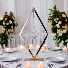 a table set with candles and plates for a formal dinner or wedding reception in front of floral centerpieces