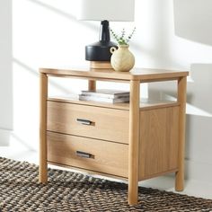 a wooden table with two drawers and a vase on top, in front of a white wall