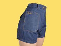 "Like new crisp dark wash twill denim shorts with a mid to high rise & short cut. To me, the fit is cute, but they're really all about the pockets! They're all flap patch pockets with buttons, but the 2 in front are so unique as the pocket can unbutton into a diagonal flap & are still accessible buttoned up. There are moderate belt loops & a robust metal zip fly with a button closure. The topstitching is burnt orange. ♡ LABELS & SIZING Made in the 70s in Thailand. There's not any branding anywhe Retro Denim Bottoms With Built-in Shorts, Vintage Jeans With Built-in Shorts For Spring, Dark Wash High-waisted Shorts With Pockets, Denim Jean Shorts With Hip Pockets, High Rise Denim Shorts With Hip Pockets, High-waisted Jean Shorts With Pockets, Dark Wash High-waisted Jean Shorts With Belt Loops, Denim High-waisted Shorts With Hip Pockets, High Waist Cotton Jean Shorts With Belt Loops