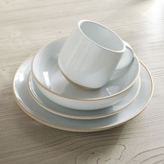 a stack of white and gold plates on top of a wooden table next to a cup