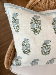 a white pillow with blue flowers on it sitting on a chair next to a wicker basket