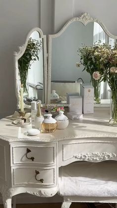 a white dressing table with flowers in vases on it and a mirror behind it