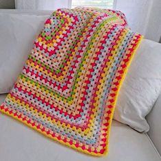 a crocheted blanket is sitting on a white couch with pillows in front of it