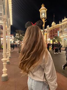 a woman with long hair walking down the street in front of mickey mouse ears at night