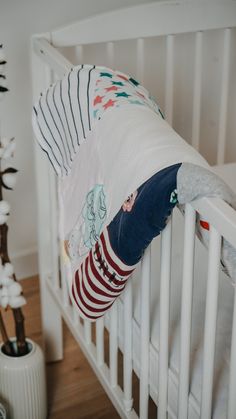 a baby laying in a crib next to a white flower pot and a plant