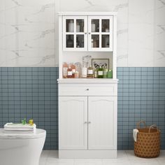 a white toilet sitting next to a cabinet in a bathroom with blue tiles on the walls