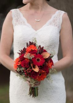 a bride holding a bouquet of red and orange flowers