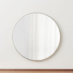 a round mirror mounted to the side of a white wall next to a wooden floor