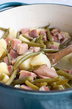 ham, green beans and potatoes in a pot with a wooden spoon on the side