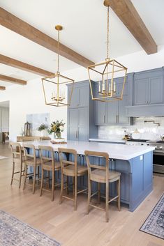 a large kitchen with blue cabinets and wooden floors is pictured in this image, there are several chairs around the island