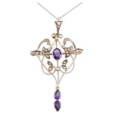 We are delighted to offer this elegant antique Edwardian art nouveau pendant necklace made c.1905. The goldwork is beautifully crafted with a naturalistic art nouveau design of scrolled foliate motifs forming an almost heart-shaped design. The pendant features two lovely faceted amethysts with a rich and regal purple hue. Further embellishments of fine seed pearls accentuate the overall appearance and create a contrast to the purple and gold tones. The bottom drop amethyst and the bail (top) mov