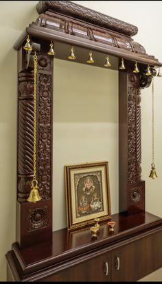 an ornate wooden mirror on top of a dresser next to a framed painting and bells