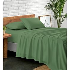 a bed with green sheets and pillows in a room next to a potted plant