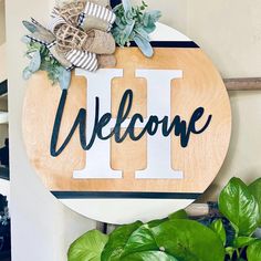 a welcome sign hanging on the wall next to a houseplant and potted plant