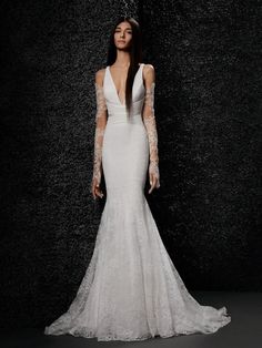 a woman in a white wedding dress standing against a black wall with her hands on her hips