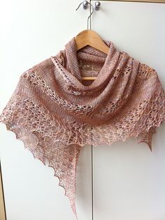 a pink shawl hanging on a white wall next to a wooden hanger with an object in it