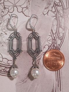 These 1920s inspired pearl dangles feature luminous white Swarovski crystal pearls that dangle from antiqued silver plated Art Deco style connectors. The silver plated connectors are brass stampings, which have an ornate front and a back that is the hollow reverse of the front. (SEE 2nd PHOTO)They are lightweight yet sturdy, and free of lead and nickel.The earrings measure 2 inches long from the top of the ear wires to the bottom of the pearl beads. They hang from silver plated lever back ear wi Art Deco Nickel-free Jewelry For Weddings, Art Deco Silver Dangle Bridal Earrings, Silver Art Deco Dangle Bridal Earrings, Silver Art Deco Bridal Earrings With Dangle Shape, Vintage Wedding Earrings With French Hook, Vintage French Hook Earrings For Wedding, Victorian Pearl Earrings For Wedding, Silver Gatsby Jewelry For Vintage Events, Art Nouveau Wedding Jewelry With Matching Earrings