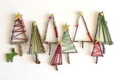 four small christmas trees made out of sticks and colored yarn are hanging on the wall