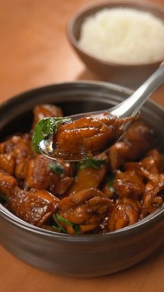 a spoon full of food sitting on top of a wooden table next to a bowl filled with rice